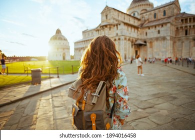 Seen from behind stylish tourist woman in floral dress with backpack having excursion near Pisa Cathedral.