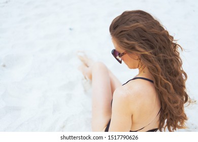 Seen From Behind Young 40 Year Old Woman In Sunglasses Sitting On Sand On A White Beach.