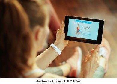 Seen From Behind Young Sports Woman In Sport Clothes In The Modern House Using Home Workout Trainer App In Tablet PC.