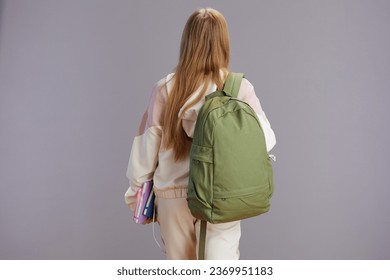 Seen from behind young woman with backpack and workbooks isolated on grey.