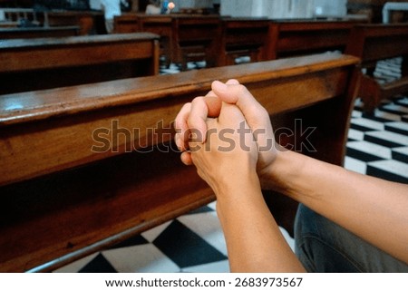 seen from the side a man keeps his fingers interlaced in prayer inside the church surrounded by benches and the patterned black and white floor