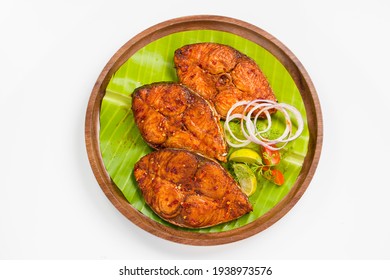 Seer fish fry arranged beautifully and garnished with onion, lemon and tomato slices on wooden plate lined with banana leaf  placed on white textured background, top view.