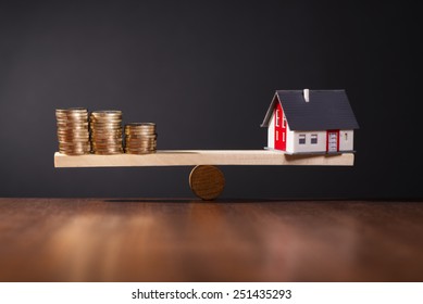 Seesaw with a house on one side and stacks of coins on the other side. - Shutterstock ID 251435293