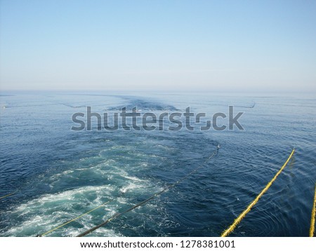 Seismic cables from industrial oil and gas researcher ship vessel in blue ocean surface, seismic seabed survey concept