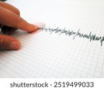 Seismograph and earthquake. A hand pointing at a seismograph recording the seismic activity of an earthquake