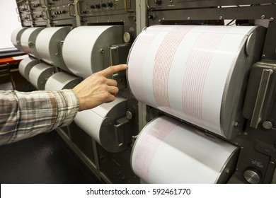 Seismograph records an earthquake on the sheet of measuring paper. Seismological device for measuring earthquakes. Earthquake wave on graph paper. Human finger showing a detail of the earthquake.