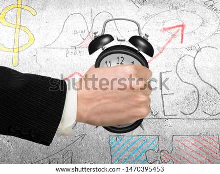 Seizing the time and present opportunities concept. Businessman hand grasping alarm clock, with business concept doodles concrete wall background.