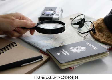 Select Destination/Women's Hand Picking A Magnifier - Stock ImageThe Device, A Map Of The World, America's Passport.Camera - Photography Equipment, Glasses, Travel Equipment, White Background Closeup