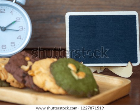 Select focus of blackboard behind of multiple color cookies inclusive peanut butter, green tea cookies, and Chocolate Chip Cookies.White clock placed in the back side