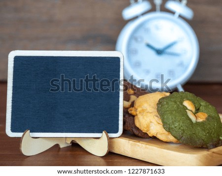 Select focus of blackboard in front of multiple color cookies inclusive peanut butter, green tea cookies, and Chocolate Chip Cookies.White clock placed in the back side