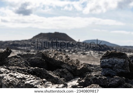 Select focus close up of pieces of lava rock in lava field near mountain Fagradalsfjall with in background out of focus fissure vent of 2021 in Geldingadalir volcano, Iceland