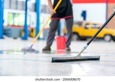 Select the focus mop, service staff man using a mop to remove water in the uniform cleaning the protective clothing of the new epoxy floor in an empty warehouse or car service center. - Powered by Shutterstock