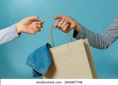 Select focus of one hand of the child is passing a craft paper bag with blue jeans to the other hand. Concept of thrift stores, resale, second hand.