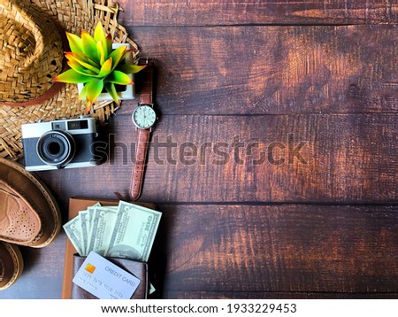 Select focus. Top view of accessories for tourist to travel in Brown tone on Travel concept, Camera on notebook and airplane with passport and money and outfit and shoes on wooden background.