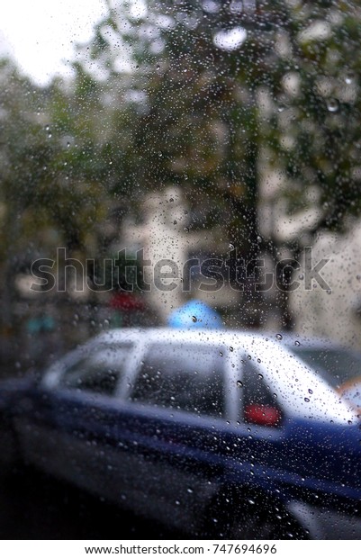 Selected background of rain drop on the glass\
window with a blur car\
outside