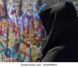 Selected Focus of a frightened woman in black dress with unrecognizable face turned back in front of a graffiti Painted Wall, Copy Space.