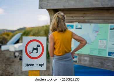 Selected Focus  Of Notice Sign For Dog Owners To Clean Up Dog Poo Excrement After Fouling Woman In Background