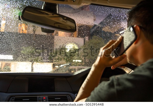 Selected focus on rain\
water drop on windshield man driving car and using cell phone while\
raining at night