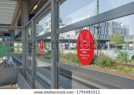 Selected focus on red circular sign for caution passenger to Keep 1.5 m distance on the glass partition at outdoor platform train Station in Germany during Social Distancing by epidemic of COVID-19.