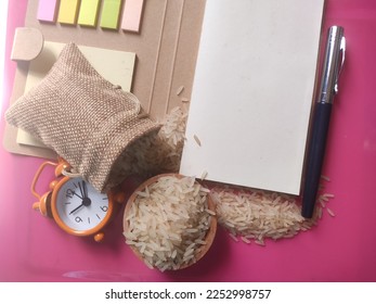 Selected focus rice in sack, bowl, clock, pen and notebook. Zakat is obligatory for Muslims and is considered an act of worship to cleanse the property acquired in a certain period and count. - Shutterstock ID 2252998757