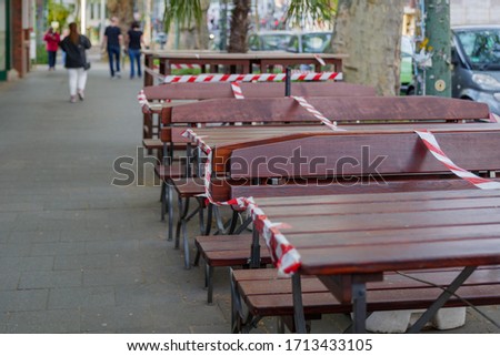 Selected focus view at Red and white caution tape wrapped around outdoor tables and seats area of cafe which closed during social distancing and global quarantine from epidemic of COVID-19 virus. 
