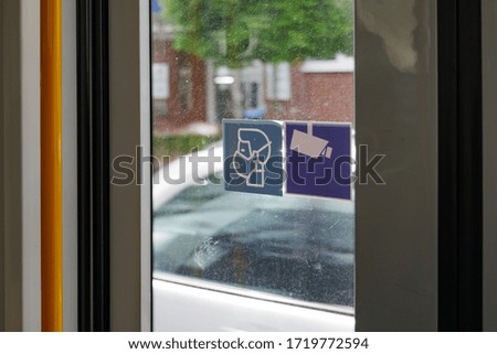 Selected focus at withe face mask covering mouth and nose on blue sign on glass of public transportation's door in Germany during epidemic of COVID-19 virus and German face mask regulations.