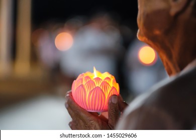 Selected focus,The wax candle in form of lotus flower on hand Old asian woman holding pray for Religious ceremony on Buddhism or make a wish in religious beliefs of buddhism.
