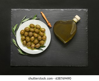 Selected olives in a white plate decorated with natural olive tree branches and olive oil heart bottle.