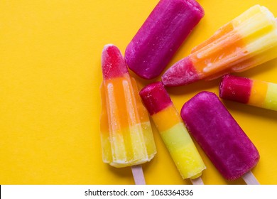 A selection of bright summer ice lollies on a yellow background