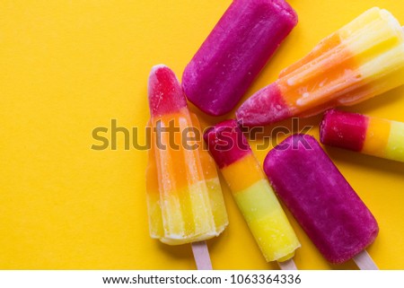 A selection of bright summer ice lollies on a yellow background