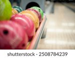 A selection of brightly colored bowling balls lined up in a rack, ready for a game at the bowling alley. 