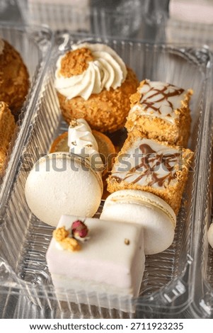 Selection of delicate mini desserts including macarons, cakes and cream pastries arranged in a clear box, perfect for bakery menus, packaging and festive promotions.