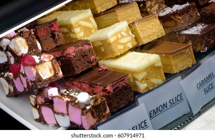 A Selection Of Delicious Cake Slices For Sale With White Labels In A Café Window