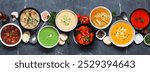 Selection of delicious homemade soups. Overhead view table scene on a dark slate banner background. Warm and cozy food concept.