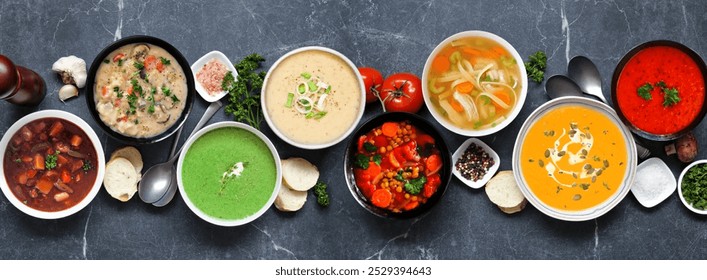 Selection of delicious homemade soups. Overhead view table scene on a dark slate banner background. Warm and cozy food concept.