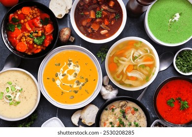 Selection of delicious homemade soups. Overhead view table scene on a dark slate background. Warm and cozy food concept.