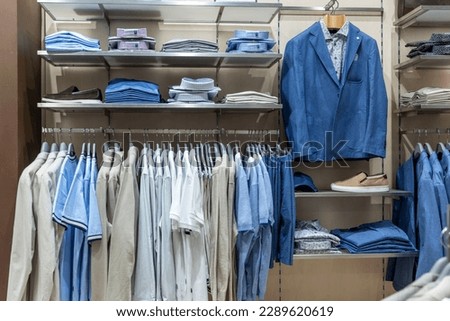 A selection of elegant business men's clothing on hangers in a store. Shirts, jackets and T-shirts on hangers. Style and fashion. Front view.