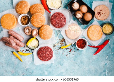 Selection Of Freshly Burger Patties, Raw Sausage And Variety Vegetables Ready To Grilled. Overhead Of Raw Grill Ingredients. Three Different Burger Meat.