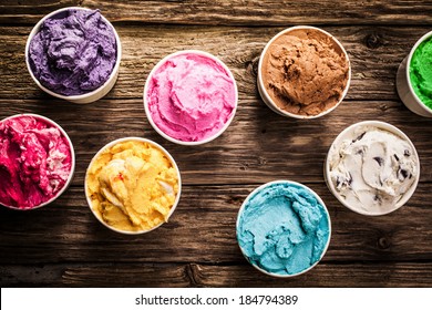 Selection of gourmet flavours of Italian ice cream in vibrant colors served in individual plastic tubs on an old rustic wooden table in an ice cream parlor, overhead view