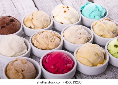Selection of gourmet flavours of Italian ice cream in vibrant colors served in individual porcelain cups on an old rustic wooden table in an ice cream parlor, angle view