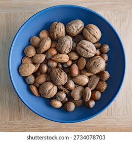Selection of mixed nuts with their shells on in a blue bowl in a table (hazelnuts, walnuts, Brazil nuts, Almonds). Heart health lifestyle vegan food. High dietary fibre. Flat lay from above.