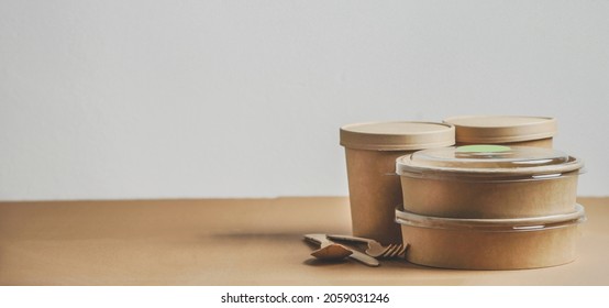 Selection Of Modern Sustainable Food Delivery Containers  And Cutlery On Kitchen Table At White Wall Background. Front View With Copy Space. Banner