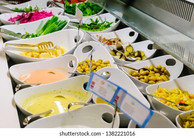 A Selection Of Olives, Chilies, Sauces And Garnishes At The Buffet Counter Of A Restaurant With A Multilingual Sign For The Sauces With Allergen Symbols