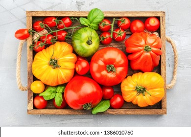 Selection of organic large heirloom and cherry tomatoes in wooden tray on light grey concrete background, top view, selective focus