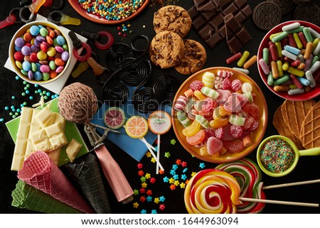 Selection of party treats for a kids birthday with assorted candies, ice cream , cookies, biscuits, chocolate bars, sprinkles and lollipops in an overhead view