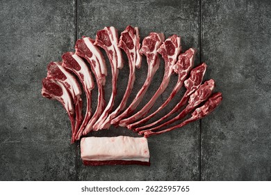 A selection of raw lamb chops and a rack of lamb laid out on a dark stone surface, showcasing fresh meat.