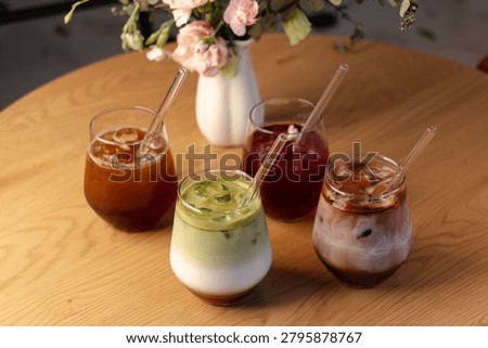 Selection of refreshing iced beverages arranged on wooden table featuring coffee tonic, berry lemonade, matcha milk and cocoa drink.