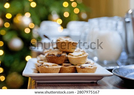 A selection of small, inviting baked goods rests on a platter, beautifully framed by the warm glow and bokeh of holiday string lights. The shallow depth of field creates a cozy, intimate atmosphere perfect for a winter celebration.