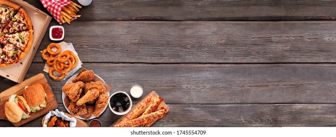 Selection Of Take Out And Fast Foods. Corner Border Banner. Pizza, Hamburgers, Fried Chicken And Sides.  Overhead View On A Dark Wood Background With Copy Space.