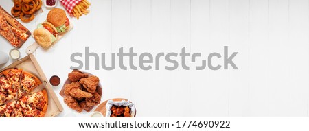 Selection of take out and fast foods. Corner border banner. Pizza, hamburgers, fried chicken and sides.  Top down view on a white wood background with copy space.